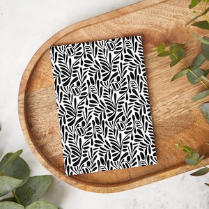 May include: Black and white notebook with a repeating pattern of stylized leaves and dots.