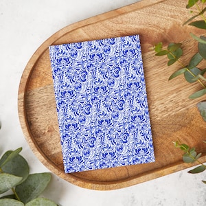 Puede incluir: Un cuaderno blanco con un patrón floral azul y blanco. El cuaderno está sobre una bandeja de madera.