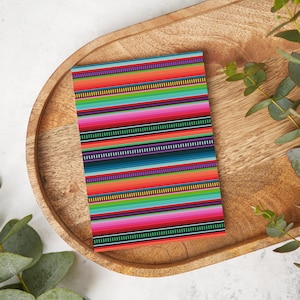 May include: A colorful striped pattern with red, orange, yellow, green, blue, purple, and black stripes. The pattern is on a piece of paper and is sitting on a wooden tray.