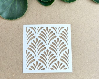 May include: White stencil with a repeating pattern of stylized leaves. The stencil is on a brown surface.