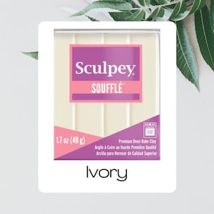 Puede incluir: Un paquete de arcilla polimérica Sculpey Soufflé de color marfil. La etiqueta dice "Sculpey Soufflé" y "1.7 oz (48 g)". El paquete también incluye texto en francés e inglés. La palabra "Ivory" está impresa en la parte inferior.