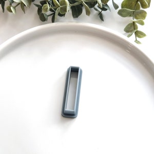 Könnte beinhalten: Ein graues Plastikrechteck mit einem rechteckigen Ausschnitt in der Mitte. Das Rechteck befindet sich auf einer weißen Oberfläche.