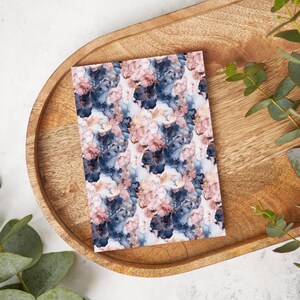 May include: A white card with a repeating pattern of blue and pink watercolor flowers with gold accents. The card is on a wooden tray.