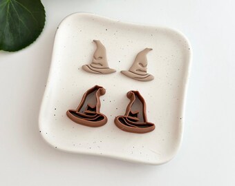 Op de afbeelding: Vier heksenhoedvormige items in twee verschillende bruintinten liggen op een gespikkelde witte keramische schaal. Dit zijn waarschijnlijk Halloween-thema knutsel- of decoratie-artikelen.