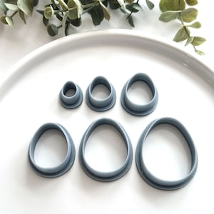 May include: A set of six gray plastic cookie cutters shaped like different sized ovals. The cutters are arranged on a white plate.