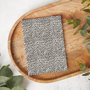 Op de afbeelding: Een klein notitieboekje met een witte achtergrond en een zwart-bruin luipaardprint.