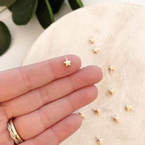 May include: A close-up of a gold star charm. The charm is small and has a simple design. It is perfect for adding a touch of sparkle to jewelry.