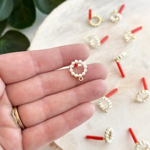 Puede incluir: Primer plano de un colgante dorado con un círculo de perlas blancas. El colgante está sobre una superficie blanca con otros colgantes similares.