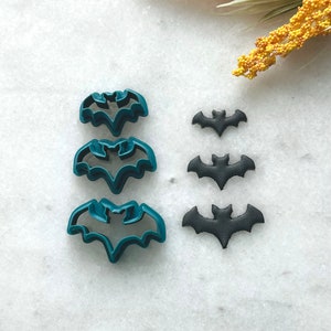 May include: Three teal blue plastic bat cookie cutters and three black plastic bat cookie cutters of varying sizes.
