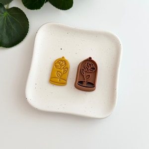 May include: Two resin charms shaped like a rose in a glass dome. One charm is brown and the other is yellow.