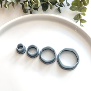 May include: Four light blue, geometric-shaped cookie cutters of varying sizes. The cutters are arranged in a row, with the smallest on the left and the largest on the right. The cutters have a wavy edge and are made of plastic.