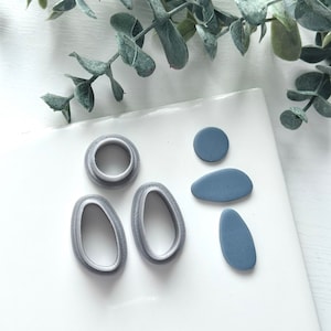 May include: A set of three gray polymer clay cutters in the shape of circles and ovals, and three blue polymer clay shapes, a circle and two ovals.