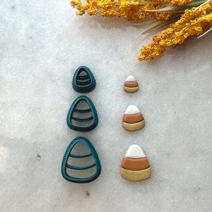 May include: Three teal blue candy corn cookie cutters and three fondant candy corn decorations. The fondant candy corn is white, orange, and yellow.