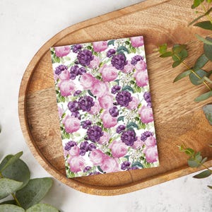 May include: A white card with a floral pattern featuring pink and purple roses. The card is on a wooden surface.