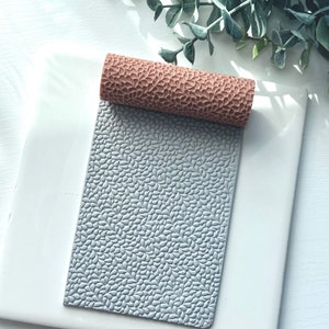 May include: A gray silicone rolling pin with a leaf pattern. The rolling pin is on a white surface.