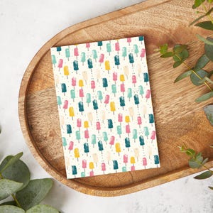 Peut inclure: Une carte blanche avec un motif répété de sucettes glacées colorées. Les sucettes glacées sont dans des tons de rose, jaune, bleu et vert. Le fond est blanc avec de petits points noirs.