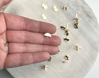 May include: Gold-toned half-circle earring findings with a jump ring. The findings are scattered on a white marble surface.