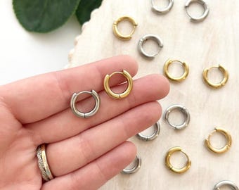 Op de afbeelding: Een verzameling kleine gouden en zilverkleurige oorringen. De oorbellen worden getoond op een lichte ondergrond, sommige worden in een hand gehouden. De oorbellen hebben een eenvoudig, minimalistisch ontwerp, geschikt voor dagelijks gebruik.