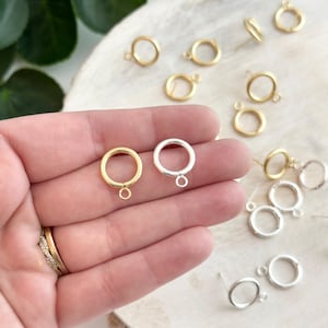 May include: Two gold and two silver jump rings with a small loop on the bottom. The jump rings are on a wooden surface.