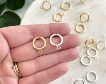 May include: Two gold and two silver jump rings with a small loop on the bottom. The jump rings are on a wooden surface.