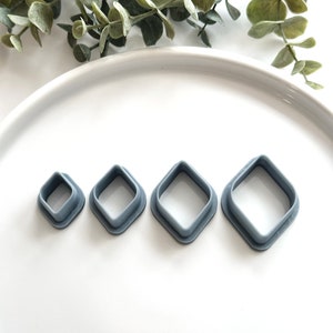 May include: Four gray plastic diamond-shaped cookie cutters of varying sizes on a white surface.