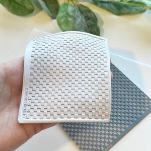 May include: A white, square, textured stamp with a checkerboard pattern. The stamp has rounded edges and the text "CHECKERBOARD" is printed on the side. A gray checkerboard stamp is in the background.