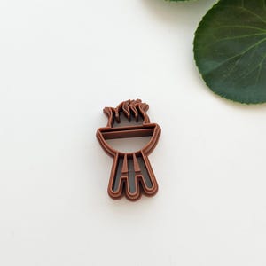 Könnte beinhalten: Ein brauner Plastik-Ausstecher in Form eines Grills mit Flammen oben drauf.