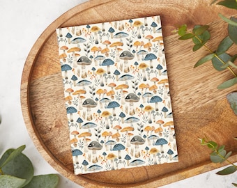 May include: A white card with a repeating pattern of blue and orange mushrooms and green leaves. The card is on a wooden tray.