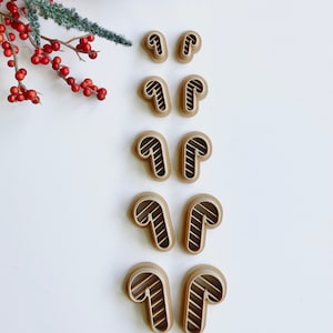 May include: A set of ten brown plastic candy cane cookie cutters. The cutters are arranged in two rows of five, with the candy canes facing the same direction in each row.