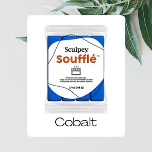 Puede incluir: Un paquete de arcilla polimérica Sculpey Soufflé azul cobalto. El paquete tiene el nombre de la marca y del producto en naranja y blanco. El paquete también incluye el peso de la arcilla, 48 g, y la palabra "Cobalt" en la parte inferior.