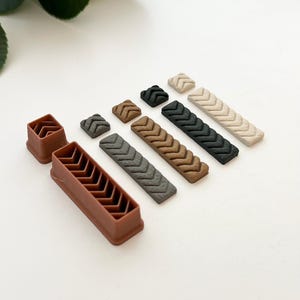 May include: A set of six polymer clay tile molds in various colors, including brown, gray, black, and beige. The molds feature a chevron pattern and are designed for creating decorative tiles.
