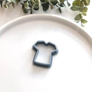 May include: A gray plastic cookie cutter shaped like a t-shirt.