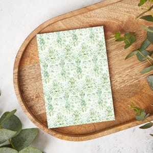 May include: A white card with a green and white damask pattern. The card is on a wooden tray with green leaves.