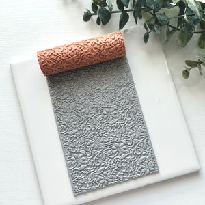 May include: A gray and brown rolling pin with a floral pattern. The rolling pin is on a white surface.