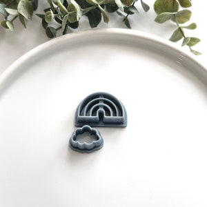 May include: A set of two gray plastic cookie cutters, one shaped like a rainbow and the other shaped like a cloud.