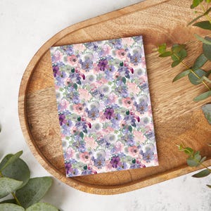 May include: A white card with a floral pattern featuring pink, purple, and white flowers. The flowers are watercolor-style and have a soft, romantic feel.