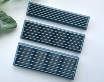 Può includere: Tre griglie di ventilazione in plastica grigia di diverse dimensioni. Le griglie di ventilazione sono rettangolari e realizzate in materiale rigido.