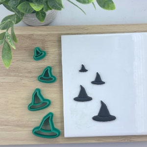 May include: A set of five green plastic witch hat cookie cutters and five black fondant witch hats on a white surface.