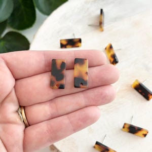 Peut inclure: Un ensemble de six boucles d'oreilles rectangulaires brunes et jaunes avec un motif en écaille de tortue. Les boucles d'oreilles sont en plastique et ont une tige argentée.