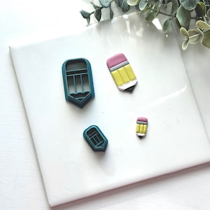 May include: Four pencil-shaped cookie cutters, two are teal blue and two are made of polymer clay. The polymer clay pencils are yellow, pink, and black.