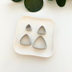 May include: Four gray plastic triangle-shaped cookie cutters of different sizes on a white speckled plate.