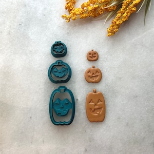 Puede incluir: Conjunto de cuatro cortadores de galletas de calabaza de color azul verdoso y marrón. Los cortadores son de diferentes tamaños y presentan una cara de calabaza.