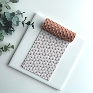 May include: A light brown silicone rolling pin with a diamond pattern. The rolling pin is on a white surface with a similar diamond pattern.
