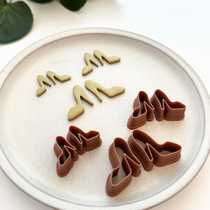May include: Two sets of high heel shoe cookie cutters. One set is gold and the other is brown.