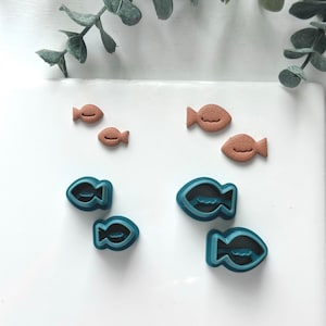 May include: A set of six fish-shaped cookie cutters, three are brown and three are blue. The cutters are arranged on a white surface.
