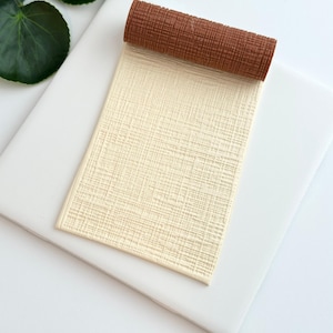 May include: A brown and cream textured silicone rolling pin for baking and decorating cakes. The rolling pin is rolled up and the textured side is facing up.