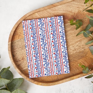 May include: A white fabric with red and blue floral patterns in vertical stripes. The fabric is on a wooden tray.