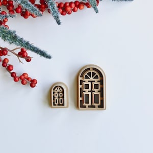 May include: Two wooden cutout window shapes with arched tops. The larger window has a grid pattern and the smaller window has a simple door design.