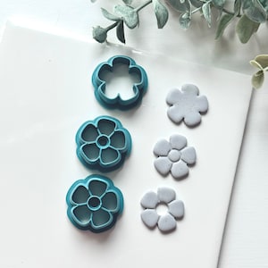 May include: A set of four blue plastic flower-shaped cookie cutters and three gray clay flower shapes.