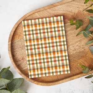 May include: A card with a checkered pattern in shades of orange, green, and white. The card is on a wooden tray with green leaves.